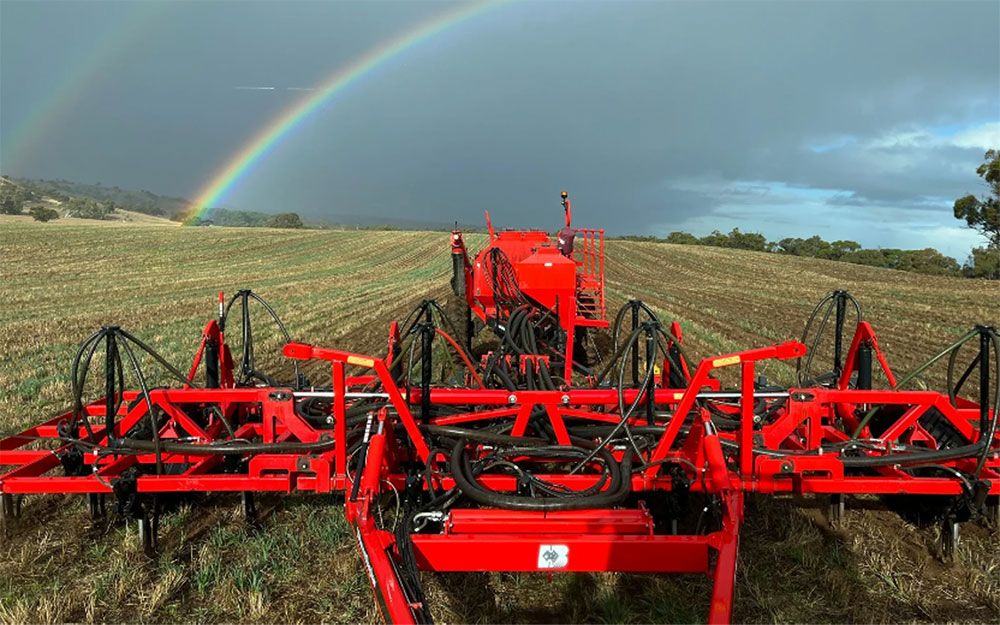 A Horwood Bagshaw Precision Seeding System in a field of stubble with a moody dark sky and rainbow in the distance